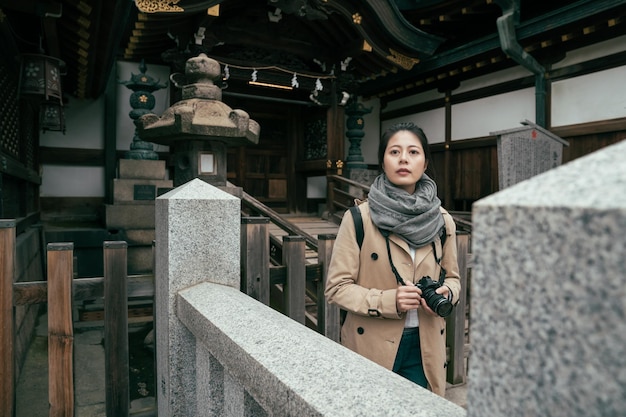 Attractive adult woman wear scarf carrying camera while relax walking in tenmangu temple. female tourist standing in japanese style stone garden in shrine. girl travel photographer visit shinto.