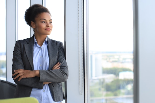 魅力的なアフリカ系アメリカ人のビジネス女性がオフィスに立って笑っています。