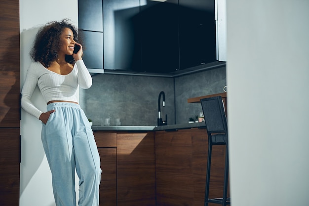 Attractive African American female spending time alone in the kitchen while talking on her phone