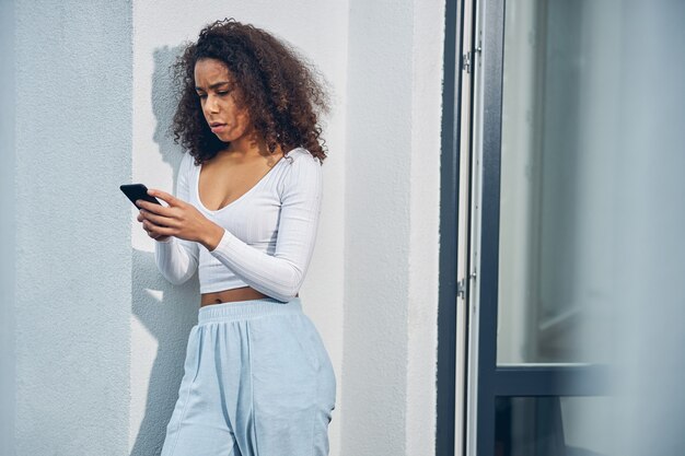 Attractive African American female standing outside alone in home clothes while holding mobile in her hands