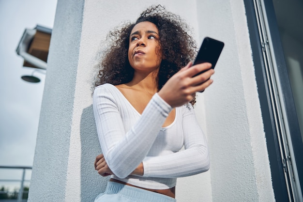 Attractive African American woman leaning against wall while holding mobile in hand