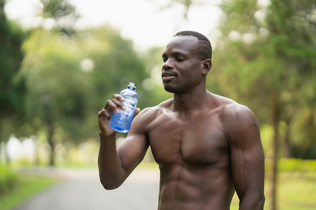 Attraente uomo sportivo africano stanco e assetato dopo aver eseguito l'allenamento con acqua potabile. concetto di uomo sportivo