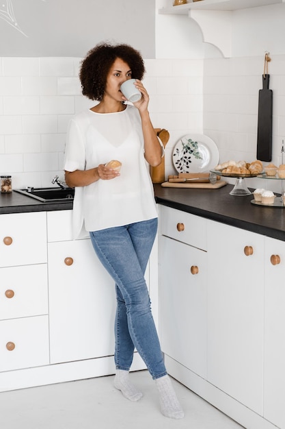 Attractive african woman with coffee and cake on the white kitchen Cozy morning of african american girl on the kitchen at home