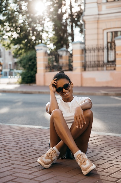 Attractive afro american woman sitting on the city street square on sunset