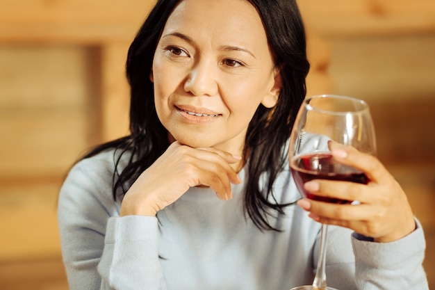 Attractive alert dark-eyed woman thinking and looking in the distance while drinking red wine