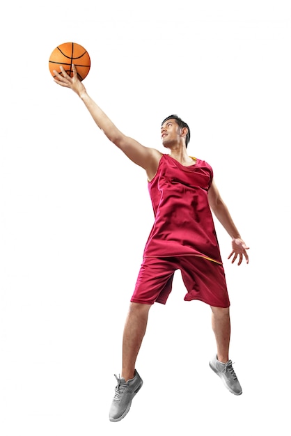 Attractive asian basketball player man in red uniform jumping with ball in hands