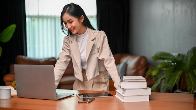 Donna di affari asiatica attraente che controlla il suo progetto sul computer portatile che esamina lo schermo del computer portatile