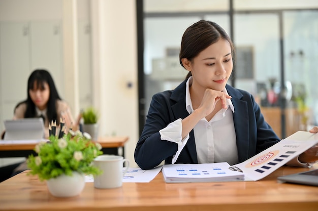 Привлекательная азиатская деловая женщина концентрируется на своем финансовом отчете за рабочим столом