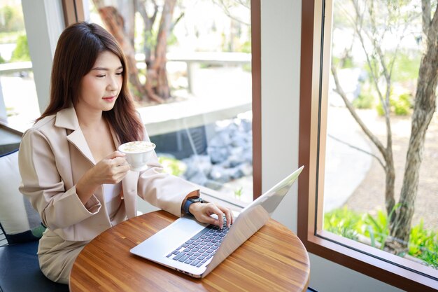 매력적인 아시아 여성 사업가가 커피를 마시고 커피숍에서 노트북으로 일하는 자신감 있고 똑똑한 여성과 비즈니스 개념