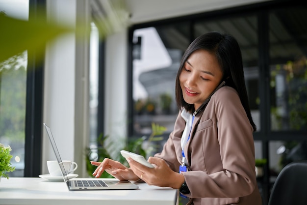 Attractive Asian businesswoman is on the phone with her business client while using calculator