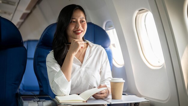 An attractive Asian businesswoman is sitting at a window seat on a plane going on a business trip