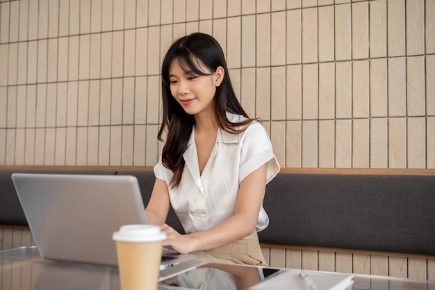 매력적인 아시아 사업가 여성이 커피에서 노트북으로 원격으로 일하고 있습니다.