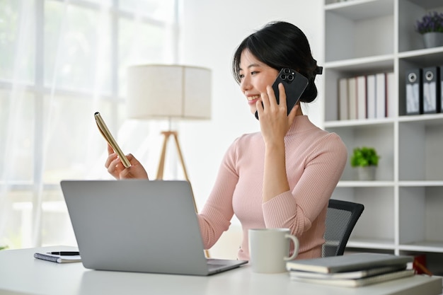 Attractive Asian businesswoman looking at the details on a notepad while talking on the phone