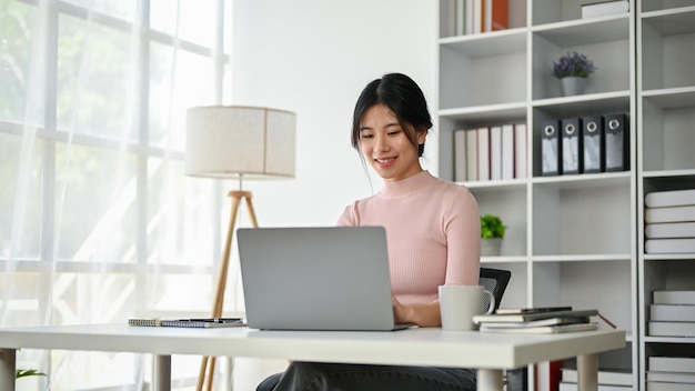 Una donna di affari asiatica attraente che esamina i suoi email di risposta dello schermo del computer portatile