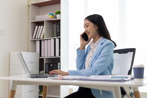 Attractive Asian businesswoman in the office is texting on a smartphone and calling with a customer on a cell phone