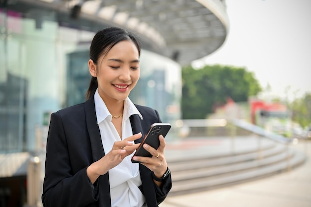 会社の建物に沿って外を歩きながら彼女の電話を使用して魅力的なアジアの実業家