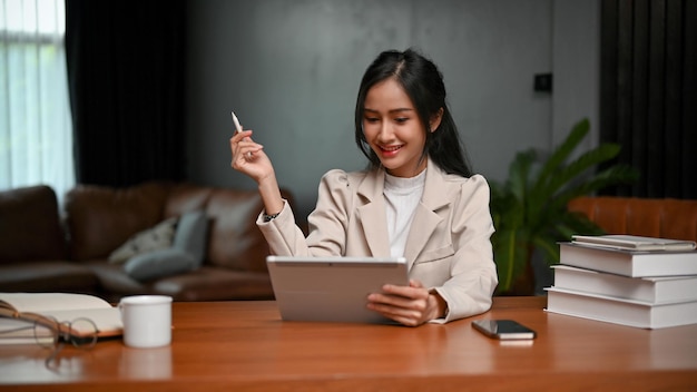 Attractive Asian businesswoman working on her business tasks on tablet in her private office