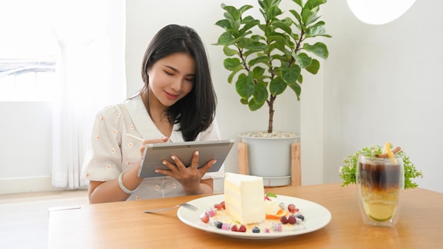 Attractive Asian female cafe blogger sitting in the cafe using tablet to update her online content