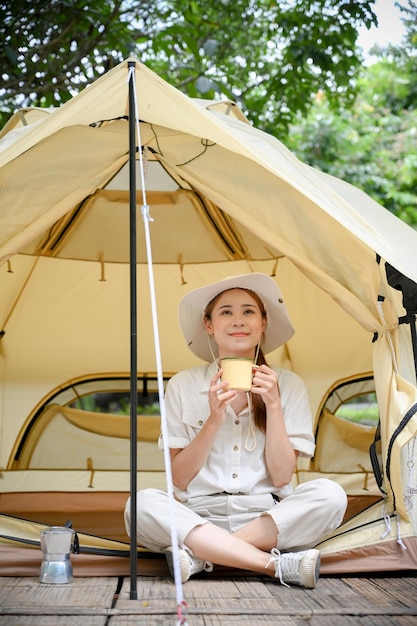 Attractive Asian female camper relaxes sitting in front of her tent having a morning coffee