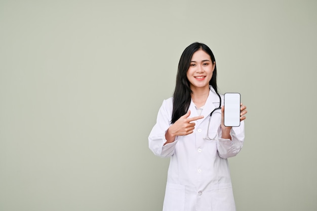 Attractive Asian female doctor in uniform pointing finger at a smartphone mockup