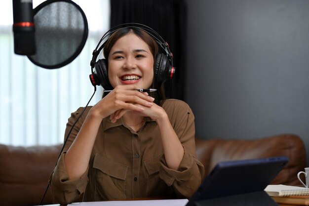 헤드폰을 끼고 있는 매력적인 아시아 여성 인플루언서가 팟캐스트를 녹음하고 방송하고 있습니다