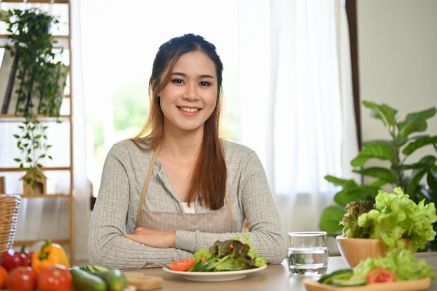 魅力的なアジアの女性が、手作りのサラダと新鮮な野菜を添えて食卓に座る