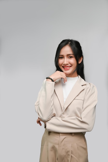 Attractive Asian female smiling hand on chin standing isolated over grey studio background