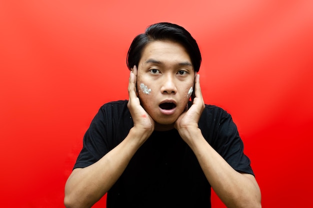 Attractive Asian Man Applying Cream on Acne Face isolated on red background. Skincare Concept.