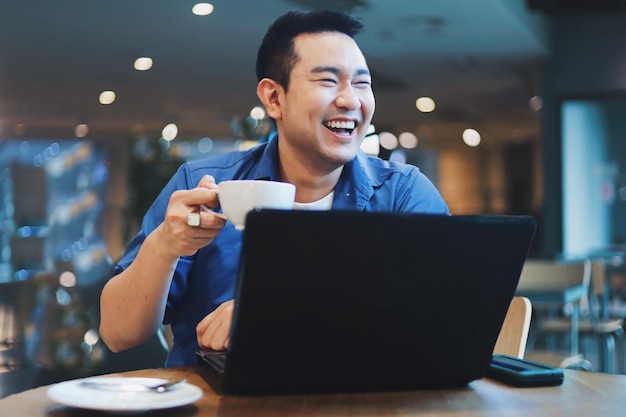 Uomo asiatico attraente in camicia blu che lavora al caffè uomo asiatico sorridente che beve caffè