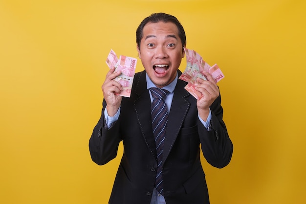 Attractive Asian man in business suit standing against yellow background showing money one hundred