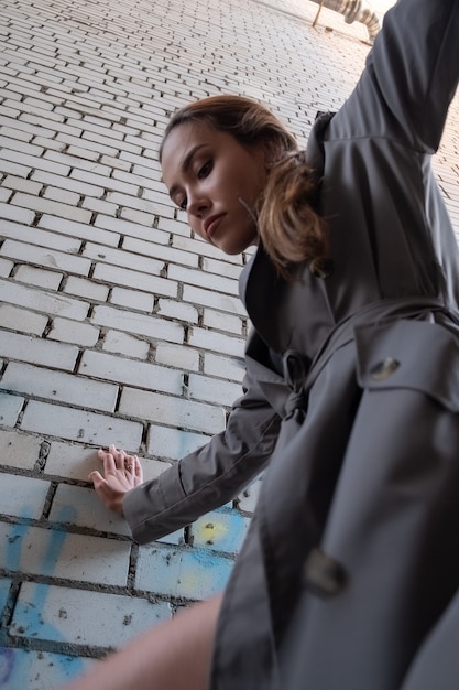 Attractive asian model in trench coat standing near wall shot from lower point