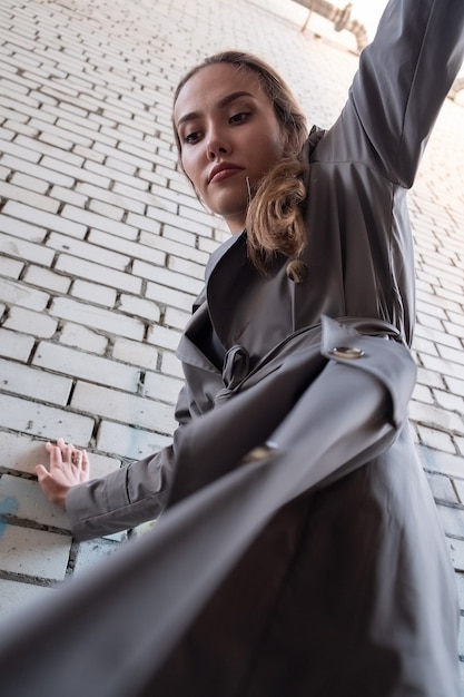 Attractive asian model in trench coat standing near wall shot from lower point