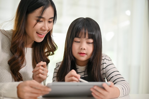 Attractive Asian mom or tutor teaching math on a tablet to a little girl at home