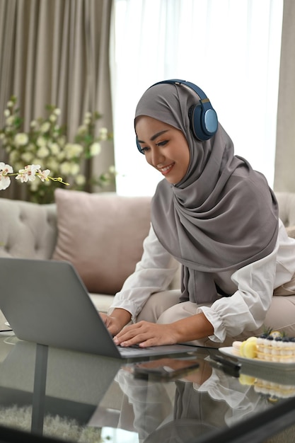 Donna musulmana asiatica attraente che utilizza un computer portatile nel suo soggiorno