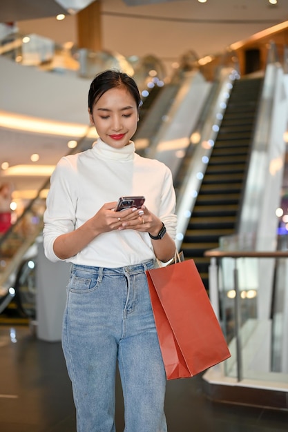 쇼핑몰에서 쇼핑하는 동안 그녀의 스마트폰에 그녀의 친구와 채팅 매력적인 아시아 여자