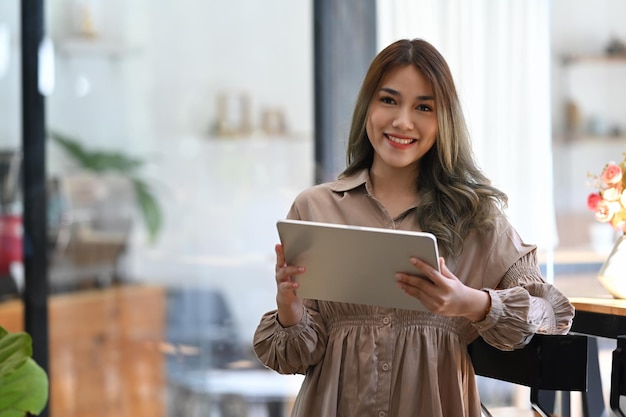 Привлекательная азиатская женщина-предприниматель, держащая цифровой планшет и улыбающаяся в камеру