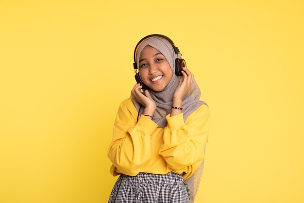 Attractive Asian woman listening music on yellow background Enjoying music