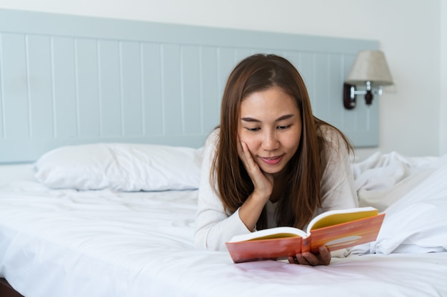 Attractive Asian woman lying down on bed reading a book.