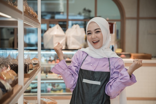 Attractive asian woman raise her arm while working at her store as a shopkeeper. muslim business owner on bakery store