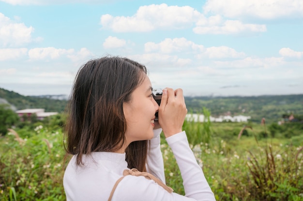 Foto attraente donna asiatica che scatta foto con una cinepresa retrò tra la natura in campagna al mattino