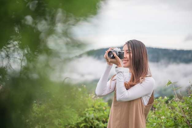 朝の田舎で自然の中でレトロなフィルムカメラで写真を撮る魅力的なアジアの女性