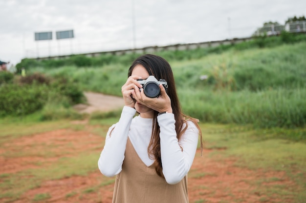 朝の田舎で自然の中でレトロなフィルムカメラで写真を撮る魅力的なアジアの女性