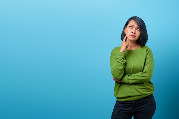 Attractive asian woman thinking and looking up empty space on blue background