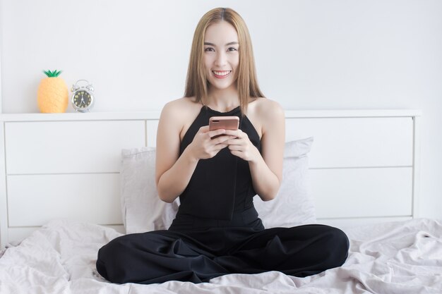 魅力的なアジアの女性はベッドでスマートフォンを使用