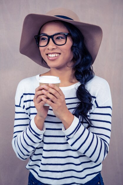 Attractive Asian woman with hat holding disposable cup and looking away