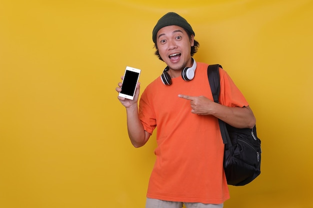 Attractive Asian young man in casual style with headphone and backpack is showing and presenting bla