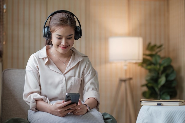 スマートフォンを使ってリラックスする魅力的なアジアの若い女性自宅のソファに座って本を読みながら遊ぶためにラップトップを使用します