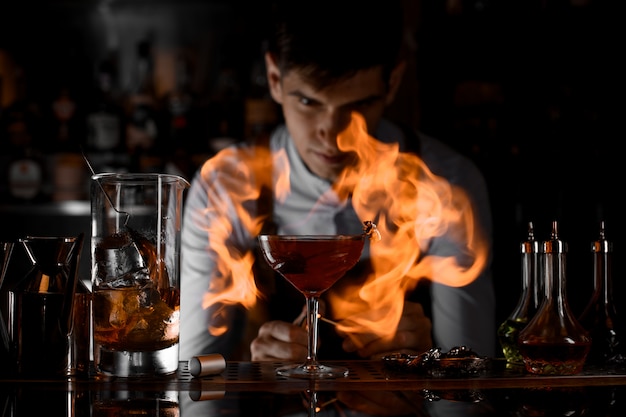 Привлекательный бармен смотрит на костер вокруг бокала для коктейля