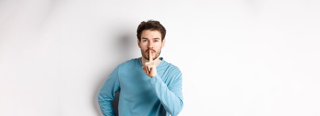 Attractive bearded man asking to keep quiet showing taboo hush gesture and looking at camera calm st