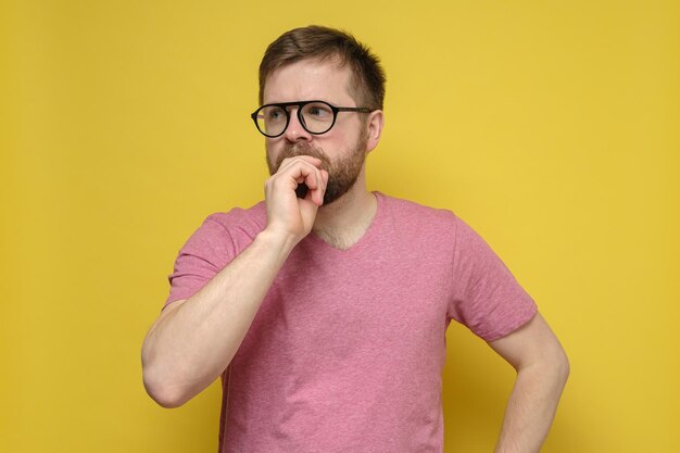 Attractive bearded man puzzled he thoughtfully looks away covering mouth with hand